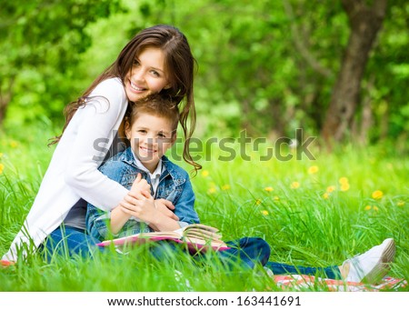 Mom and son with book sitting on green grass in green park. Concept of happy family relations and carefree leisure time