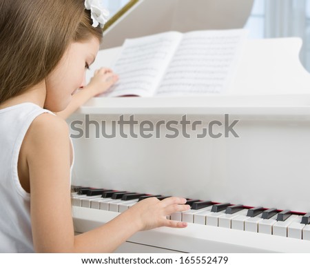 Side view of little girl in white dress playing piano. Concept of music study and arts