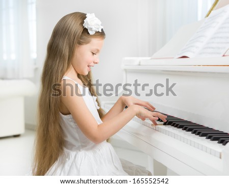 Profile of little girl in white dress playing piano. Concept of music study and art