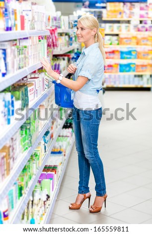 Full length portrait of girl at the shop choosing cosmetics among the great variety of products. Concept of consumerism, retail and purchase