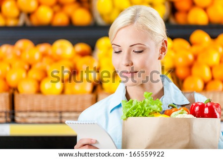 Reading list of products girl hands bag with fresh vegetables against the shelves of fruits in the shop