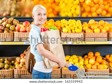 Girl with cart hands bag with fresh vegetables against the shelves of fruits in the market