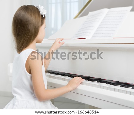 Side view of little girl in white dress playing piano. Concept of music study and art