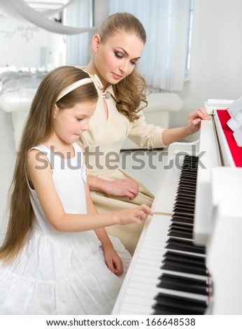 Tutor teaches little girl to play piano. Concept of music study and creative hobby