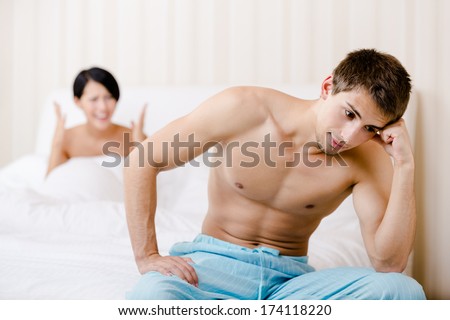 Married couple quarrels in bed. Depressed man sitting on the edge of the bed, focus on man