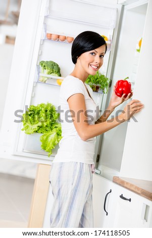 Lady takes red pepper from the opened fridge full of vegetables and fruit. Concept of healthy and dieting food