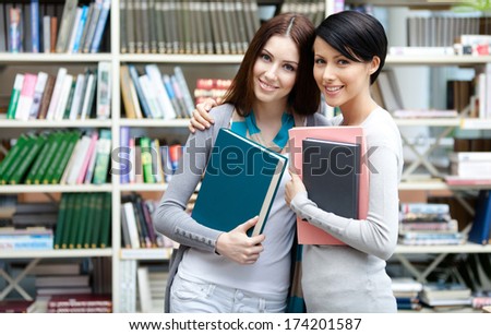 Two girlfriends keeping books hug at the library. Friendship