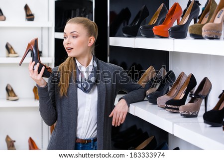 Woman with shoe in hand chooses high heeled shoes looking at the shelves with numerous heeled shoes
