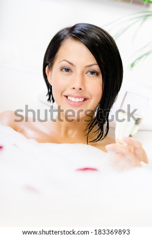 Woman taking a bath with suds and rose petals drinks champagne and relaxes