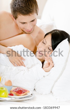 Lying man serves woman breakfast in bed. Concept of love and affection