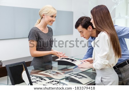 Salesperson helps couple to select jewelry at jeweler\'s shop. Concept of wealth and luxurious life