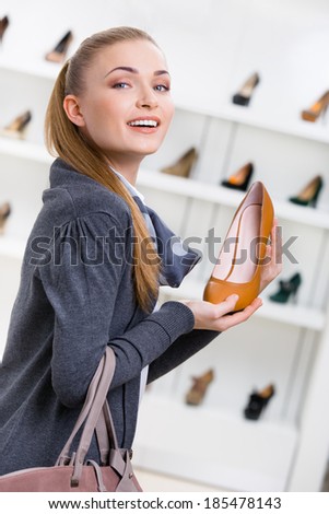 Portrait of woman keeping brown leather shoe in shopping center against the showcase with pumps