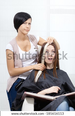 Hair stylist tries lock of dyed blond hair on the client sitting on the chair in the hairdresser\'s