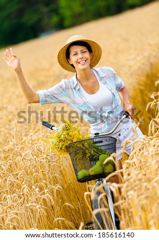 Girl pedals bicycle and waves hand in rye field. Concept of rural lifestyle and sport