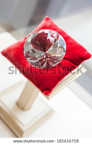 Close up of large diamond on red pillow at jeweler\'s shop. Concept of wealth and luxurious life