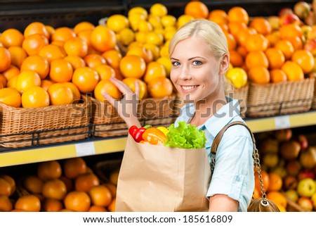Choosing oranges girl hands bag with fresh vegetables against the shelves of fruits in the shop