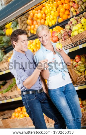 Couple with shopping list against the piles of fruits decides what to buy
