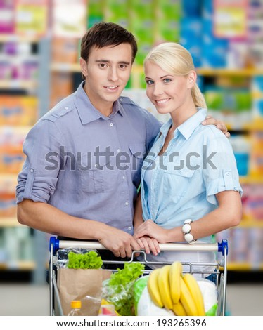 Half-length portrait of couple in the store with cart full of food. Concept of consumerism and healthy food