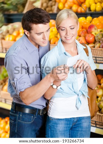 Couple with shopping list against the heaps of fruits decides what to buy