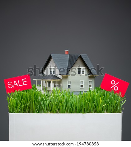 Close up of house model with green grass and sale tablet on grey background. Concept of real estate and sales