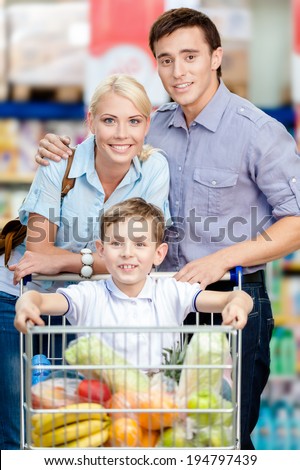 Family drives shopping trolley with food and son sitting there. Concept of fresh and healthy food and consumerism