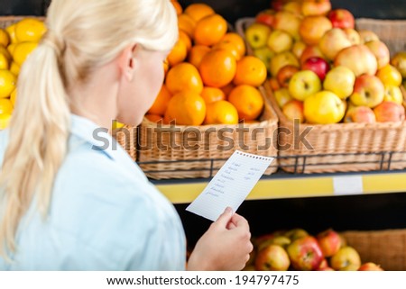 Girl reads shopping list near the heap of fruits lying in the braided baskets in the store