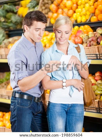 Happy couple with shopping list against the stacks of fruits decides what to buy