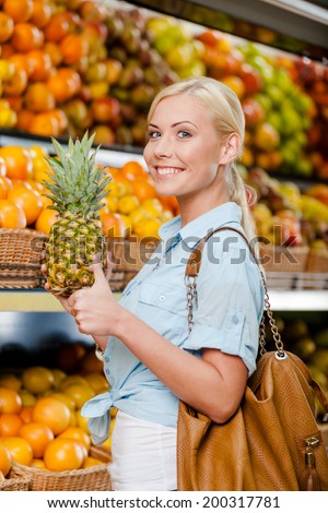 Girl at the shop choosing fruits and vegetables hands pineapple thumbs up