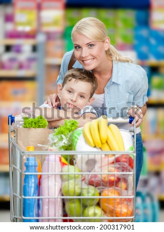 Mother and son with cart full of products in market. Concept of healthy food and consumerism