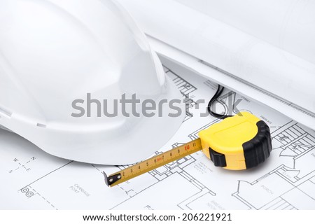 White hard hat and tape measure are on the opened design druft