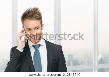 Half-length portrait of businessman speaking on cell phone against window with urban view. Concept of communication and business