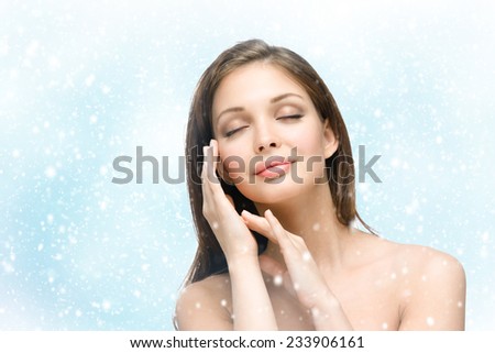 Portrait of beautiful girl with eyes closed touching face with hands, snowy background. Concept of beauty and youth