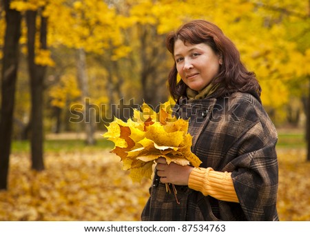 woman in the park, with a bouquet of autumn leaves and looks at the viewer smiling
