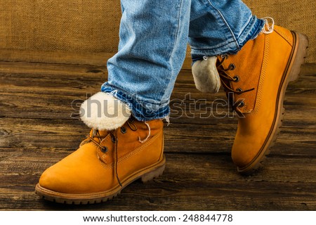 female feet in winter boots and jeans  on wooden background