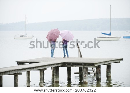 Germany, Bavaria, Ammersee two Women standing on jetty holding umbrellas rear view