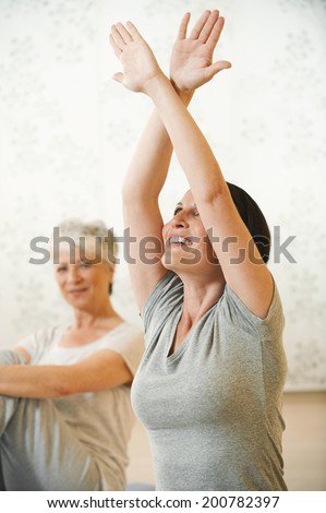 Woman sitting in gym stretching arms senior woman sitting in background