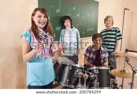 Students at music class girl clapping smiling boy playing drums classmates standing behind