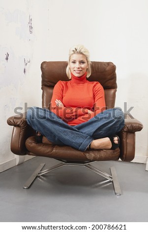 young woman sitting with crossed legs in armchair relaxing smiling