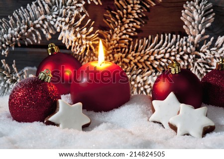 Christmas bulbs cinnnamon stars pine twig candle on pile of snow against wooden wall