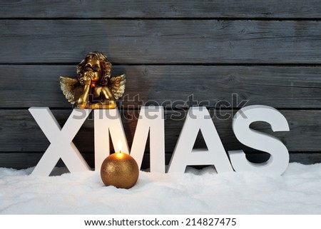 Capital letters forming the word xmas golden putto figurine and candle on pile of snow against wooden wall