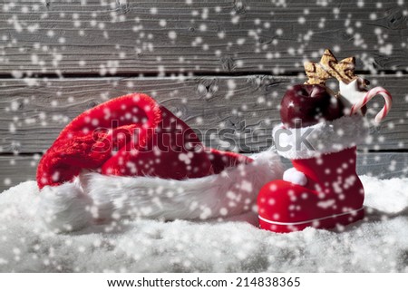 Snowfall with christmas hat and boot on heap of snow against wooden background