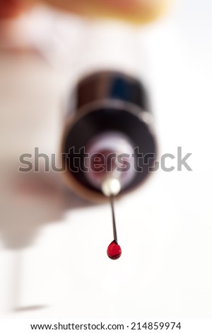 Syringe filled with blood sample drop at needle\'s top white background close up
