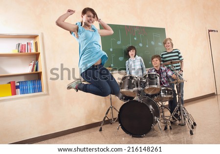 Students at music class girl jumping smiling boy playing drums classmates standing behind
