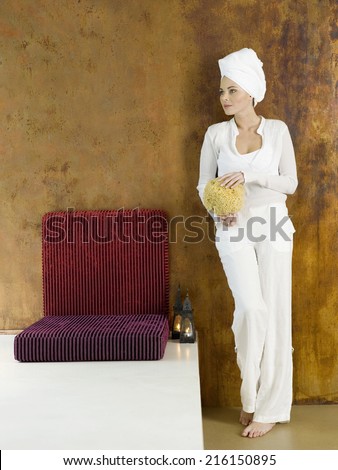 Woman standing with sponge, head wrapped in towel, looking away