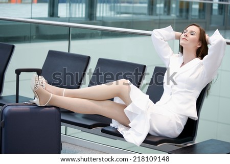 Woman sitting in waiting hall, feet on suit case