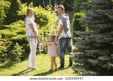 Young family, mother father and daughter walking hand in hand in garden