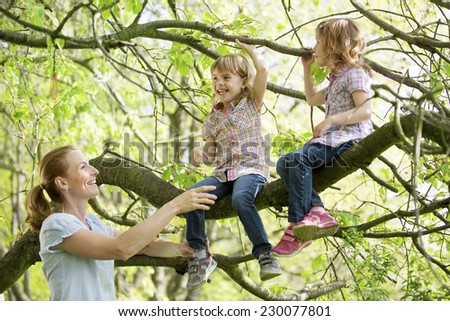 Mother helping twin girls climbing on tree