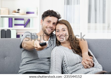 Young happy couple watching TV holding remote control
