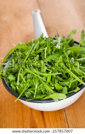 Rocket salad in a strainer on wooden table