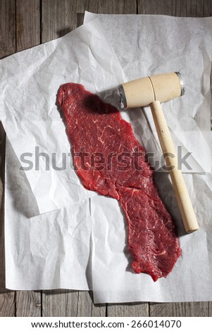 Row beef roulade and meat tenderizer on greaseproof paper and wood